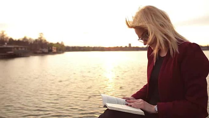 美丽的金发女人在湖边看书