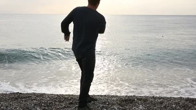 一名男子沿着荒芜的海滩走向大海，跳过岩石