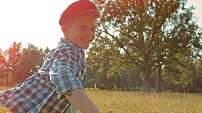 SLO MO TS肖像，一个小男孩在阳光下在草地上奔跑