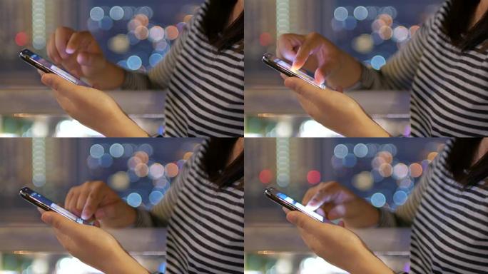 女人在夜晚用城市的圆形bokeh灯在屋顶上触摸智能手机