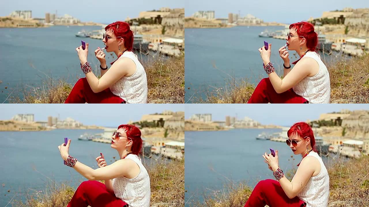 美丽的红发女孩在海边的嘴唇上涂口红