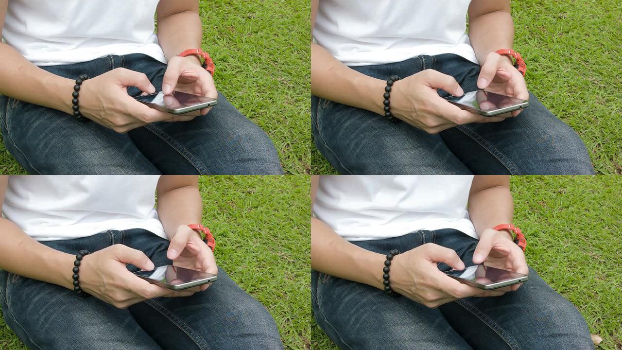 一个拿着智能手机的年轻人坐在草地上。