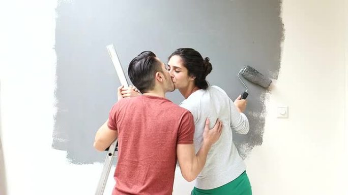 情侣在用油漆滚筒粉刷墙壁时接吻
