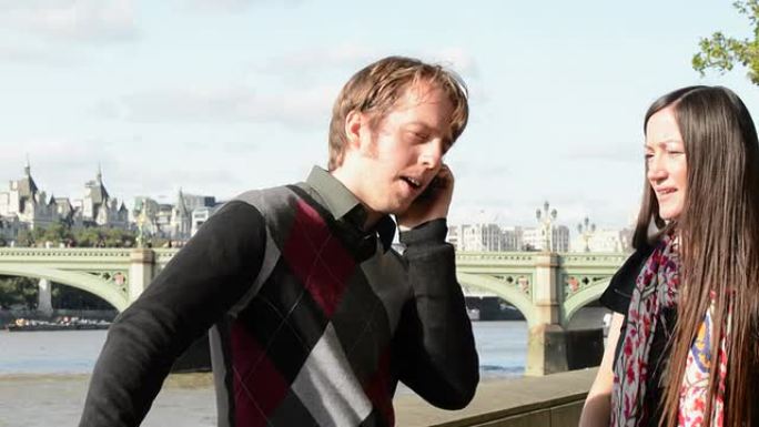 一对夫妇走在伦敦泰晤士河堤岸上，电话铃响了