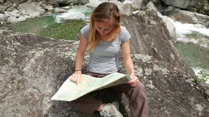 女徒步旅行者在山河边查看地图
