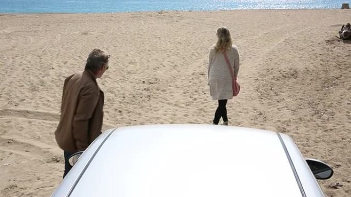 夫妇离开汽车，穿过海滩走向大海