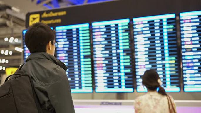 男人和女人看着航空公司的航班起飞板