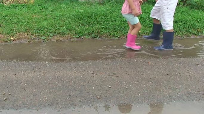 穿着五颜六色雨靴的孩子们踩着泥坑。