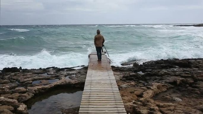 一名男子沿着海面上的木板路走着，望着远方
