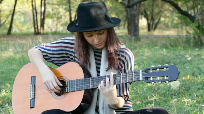 夏天，一位戴着黑色帽子的年轻女子在公园里弹吉他。