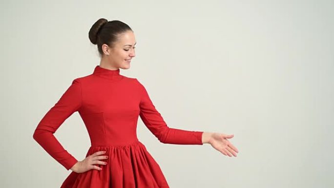 穿着红色连衣裙的美丽年轻女孩展示了复制空间，并在灰色背景上交叉双臂