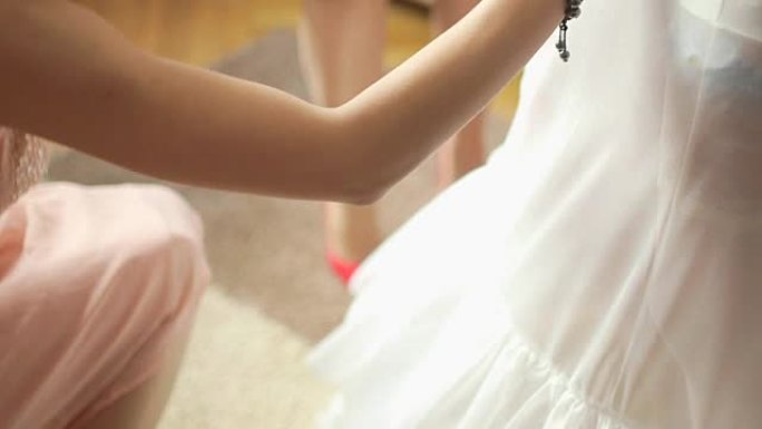 女人打扮新娘的俯身镜头。女性扣子婚纱的裁剪图像。她正在系夹克的珍珠纽扣。