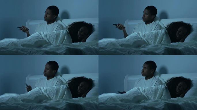一对年轻的非裔美国夫妇在床上看电视