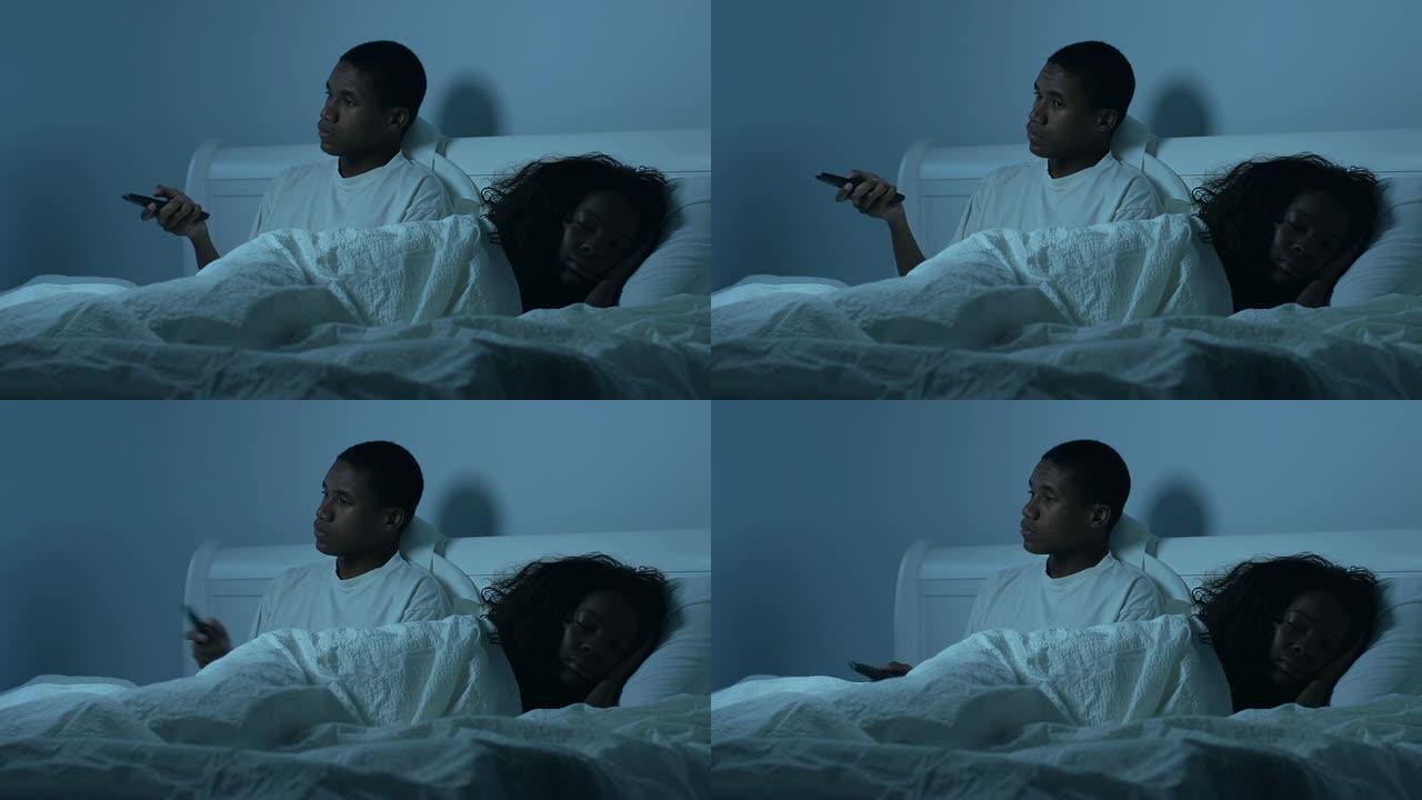 一对年轻的非裔美国夫妇在床上看电视