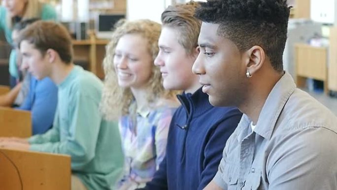 一名非裔美国青少年高中生走到一排电脑前，坐下来学习
