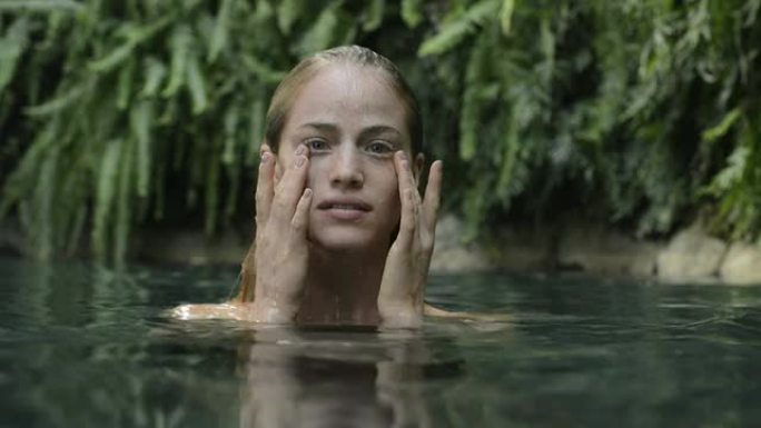 一名女子在天然水池中抚摸自己的脸