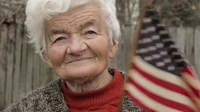 老妇人拿着美国国旗，看着相机微笑