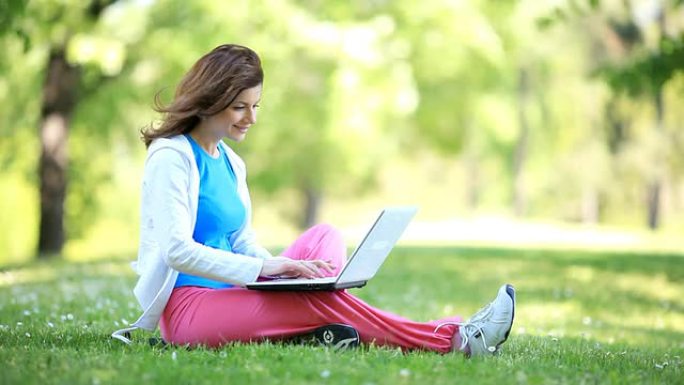 微笑的年轻女子在公园里用笔记本电脑打字。