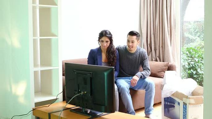 一对年轻夫妇一边看液晶电视一边聊天
