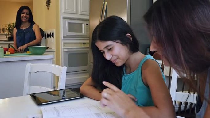 青春期的西班牙裔女孩在母亲准备晚餐时在大姐姐的帮助下做作业