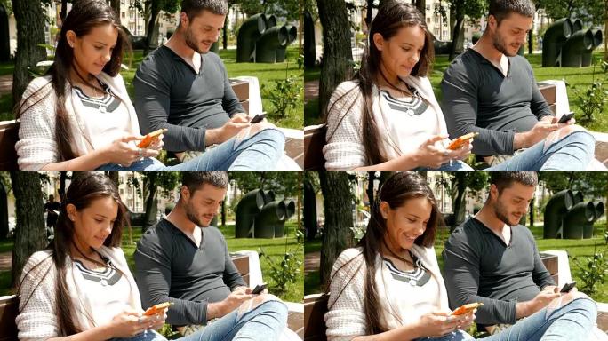 年轻的男人和女人坐在城市公园的长凳上，使用他们的智能手机
