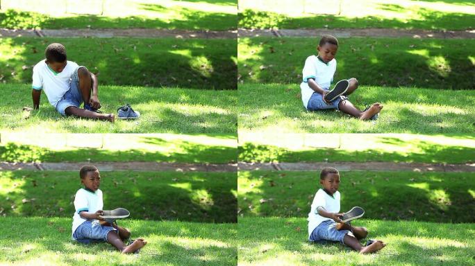 小男孩坐在草地上脱下鞋子