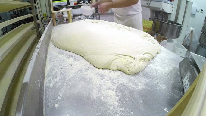 面包师在工作台上的发酵面团上撒面粉