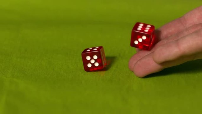 手在绿色桌子上滚动两个红色骰子