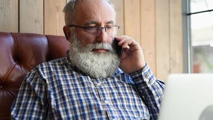 年长的大胡子男人在用智能手机说话