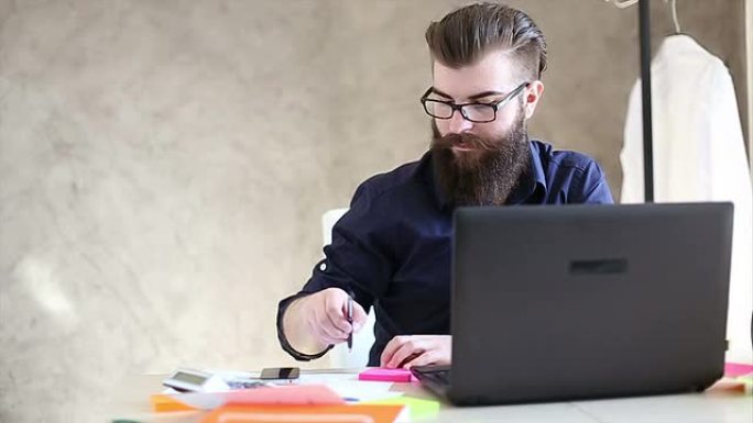 英俊的时髦胡子男子在办公室里用电脑工作