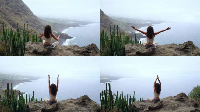 年轻女子在岛上的山上做瑜伽，俯瞰大海，坐在山顶的一块岩石上，以莲花的姿势冥想