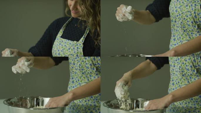 倾斜一个三十多岁的微笑的白人妇女用围裙将面粉撒在金属搅拌碗中