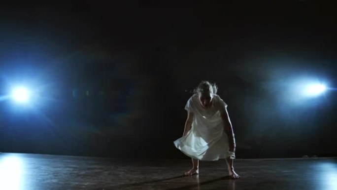 一名年轻的女芭蕾舞演员赤脚跳上舞台，穿着宽松的白色连衣裙慢动作