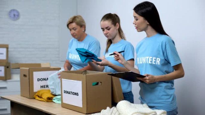 志愿者将衣服放在捐款箱中，微笑的社工做笔记