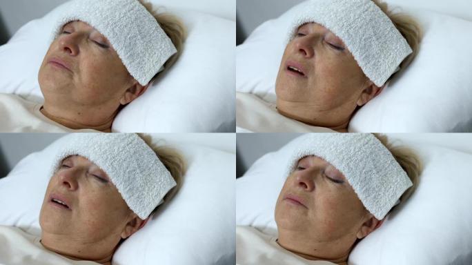 生病的老妇人额头上有毛巾躺在床上，患有感冒或流感