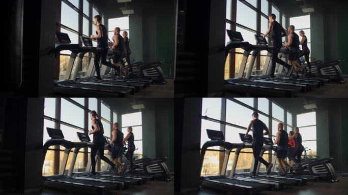 两名男子在健身室一个大窗户的背景下在跑步机上跑步。在健身室跑步的年轻人。在健身房进行有氧运动
