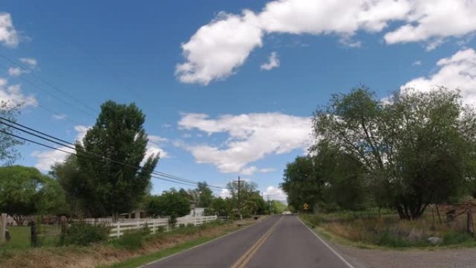 在多云的天空下，在城镇的农村居民区中沿着树木状道路行驶的车辆的移动过程板