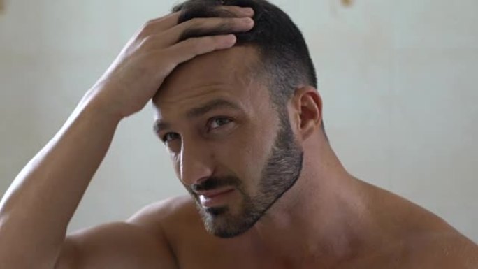 不快乐的男人在浴室的镜子前检查易碎的头发，头皮屑