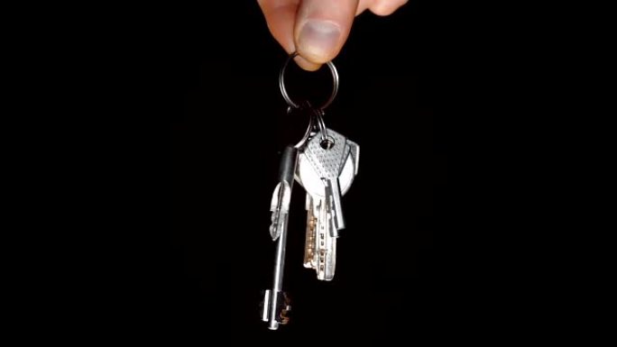 黑色背景上男性手中的一堆闪亮的镀铬公寓钥匙