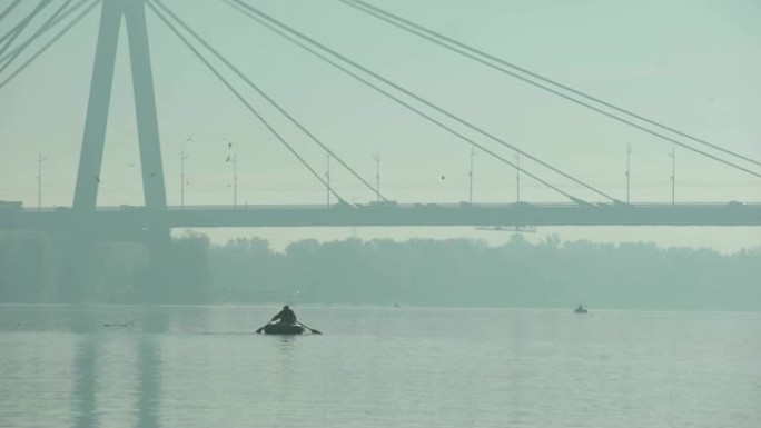 渔夫乘坐充气船在大桥下航行，雾蒙蒙的天气，大城市
