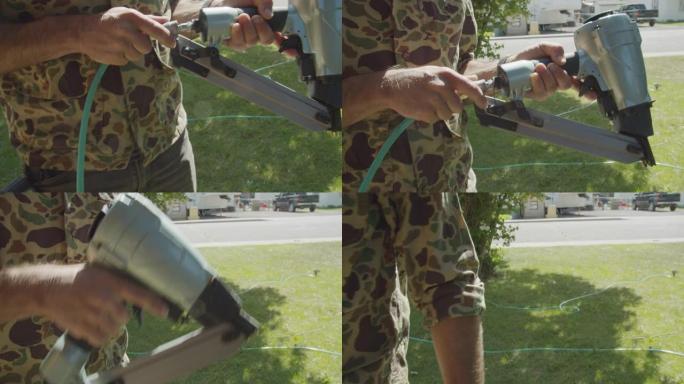 在阳光明媚的日子里，一名高加索杂工将空气软管连接到户外居民区的气动钉枪上