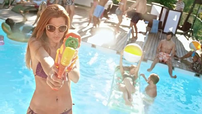 在泳池派对上，SLO MO年轻女子在用水枪将水射向镜头时大笑