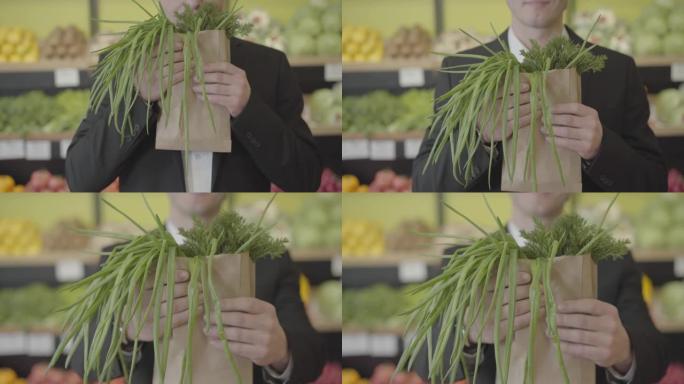 面目全非的高加索人在纸包中闻到了莳萝和葱的味道，并将一堆绿色植物伸向相机。不知名的男性顾客在杂货店购