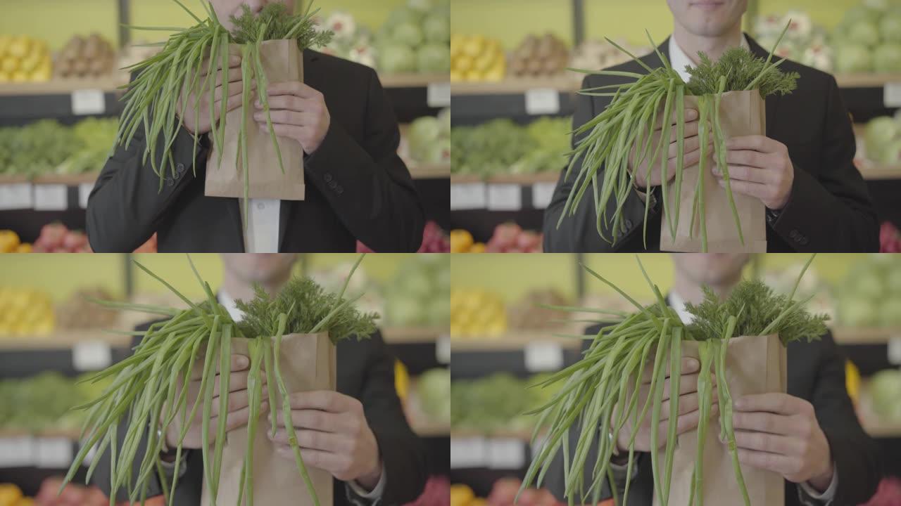 面目全非的高加索人在纸包中闻到了莳萝和葱的味道，并将一堆绿色植物伸向相机。不知名的男性顾客在杂货店购