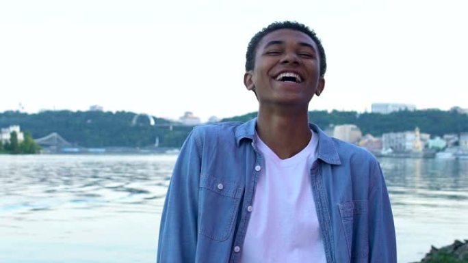 黑人少年男孩笑着真诚地站在城市景观上，享受生活
