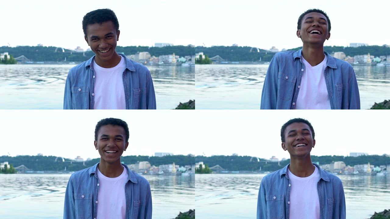 黑人少年男孩笑着真诚地站在城市景观上，享受生活