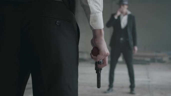 一个穿正装的野蛮人站在另一个手里拿着枪抽烟的人对面。