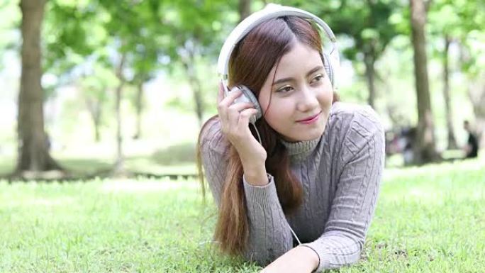 亚洲妇女躺在公园里，用耳机听音乐