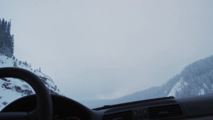 一名白人男子手放在方向盘上，在科罗拉多州落基山脉的70号州际公路上行驶，冬天在一片漆黑的阴云密布的天