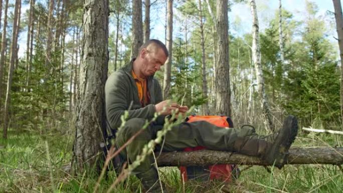 男性荒野生存专家在森林的树干上编织干草